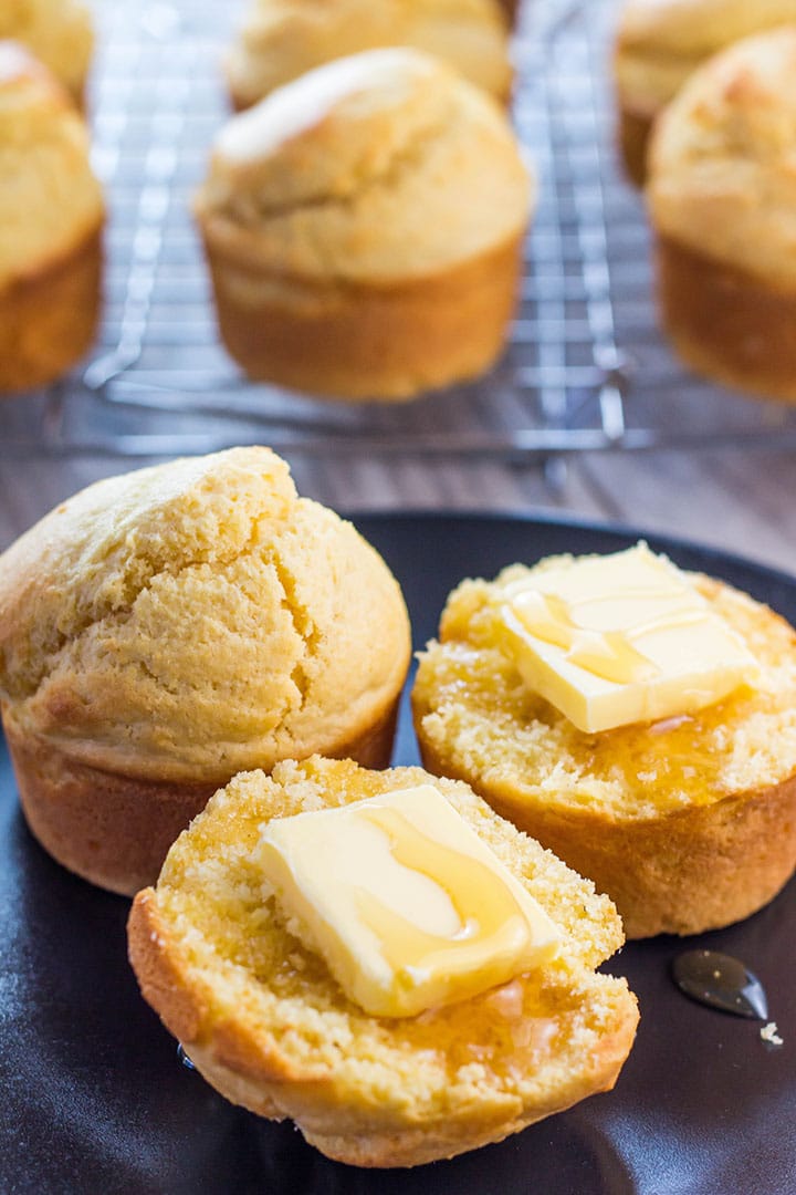 A plate of corn muffins with one cut in half with butter and honey drizzled over it