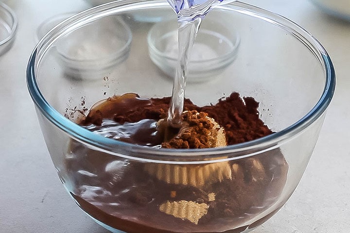 water being added to a glass bowl with cocoa powder, instant coffee and brown sugar