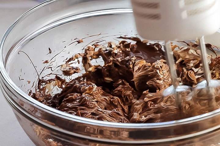 softened butter, cream cheese and melted chocolate being beat together in a glass bowl