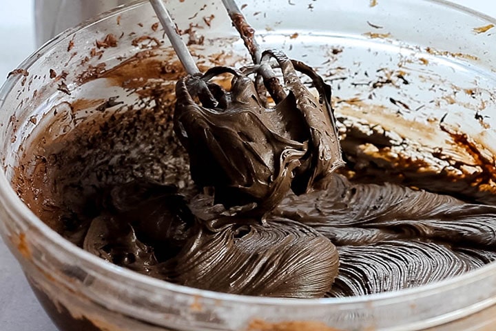 A bowl with the dark chocolate icing being mixed with a mixer