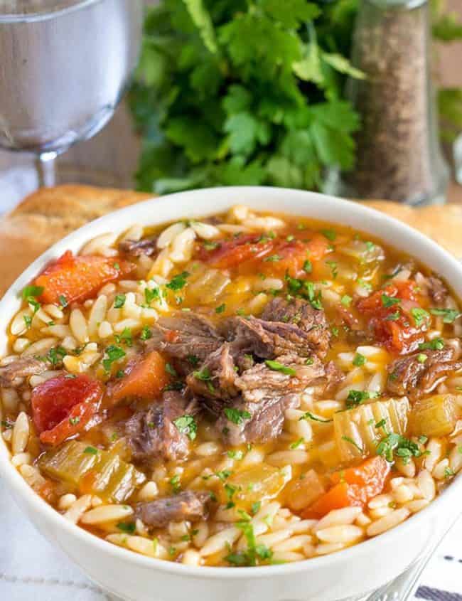 a bowl of slow cooker oxtail orzo soup with fresh herbs in the background