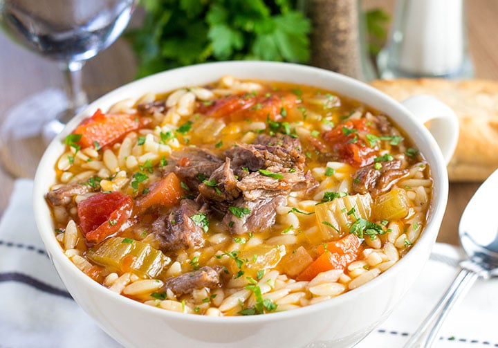 a bowl of slow cooker oxtail orzo soup with fresh herbs in the background