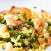 A slose up photo of a plate piled high with yellow rice, asparagu and plump shrimp