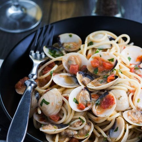 Spaghetti with Clam Sauce served on a pplate with the clams still in their shells and a fork next to the dish