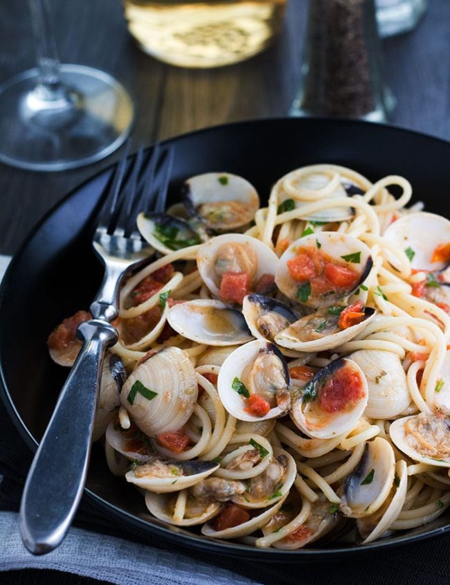 Spaghetti with Clam Sauce served on a pplate with the clams still in their shells and a fork next to the dish