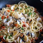 a pan with Spaghetti with Clam Sauce with the clams still in their shells speckled with green parsley and res chopped tomatoes