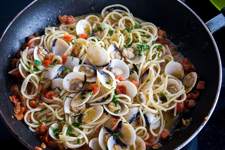 a pan with Spaghetti with Clam Sauce with the clams still in their shells speckled with green parsley and res chopped tomatoes