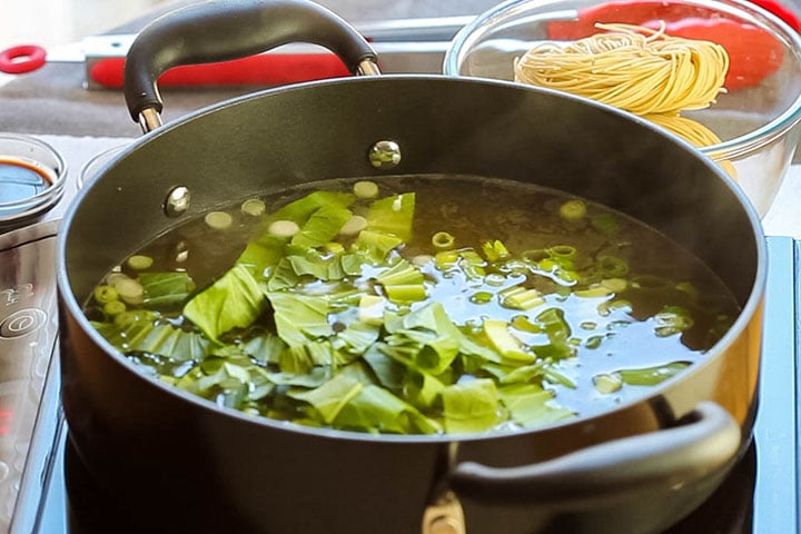 the green onions and Chinese greens added to the stock in the pot