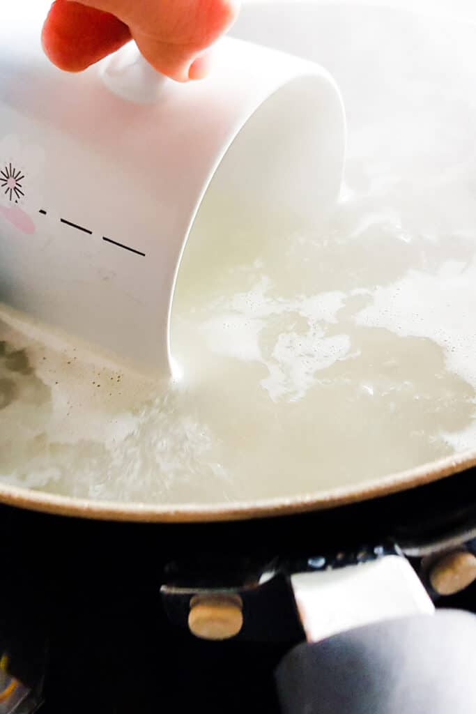 a mug scooping out some cooking water from the pot of pasta