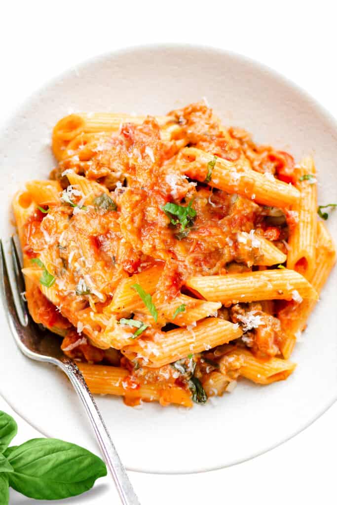 an overhead image of a bowl of pasta alla norma with a fork and basil leaf
