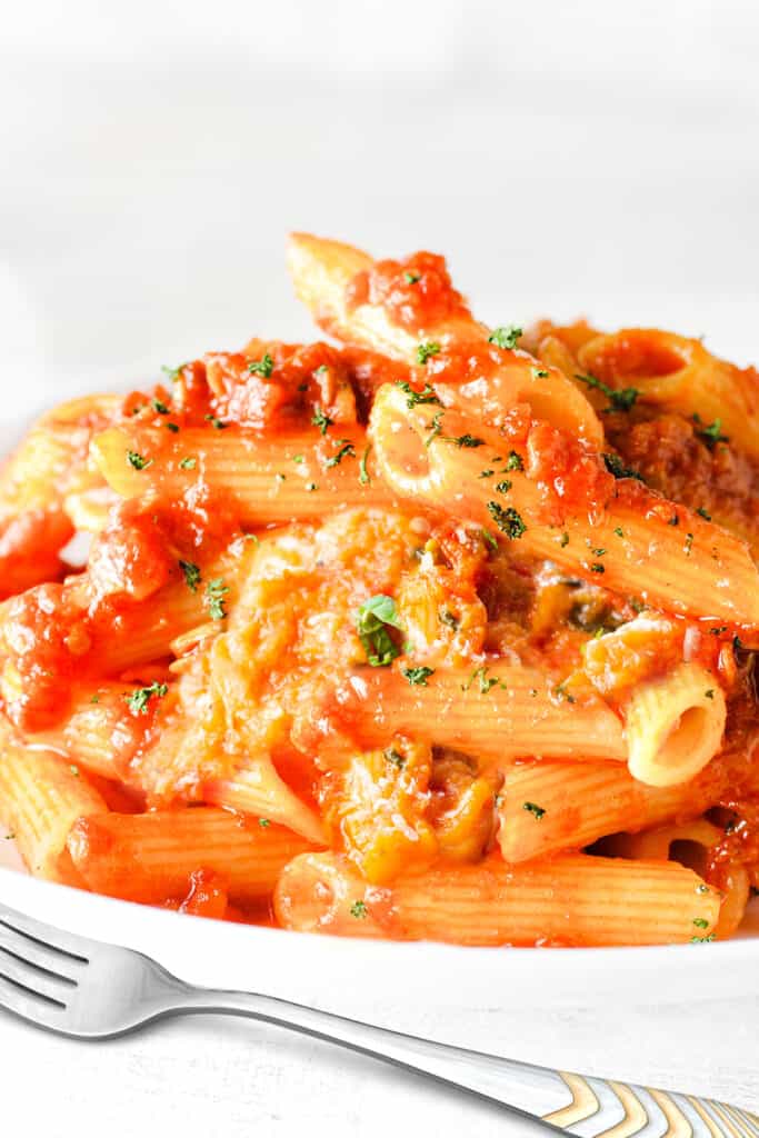 A big plate of Pasta Alla Norma sprinkled with cheese and scattered with sliced basil