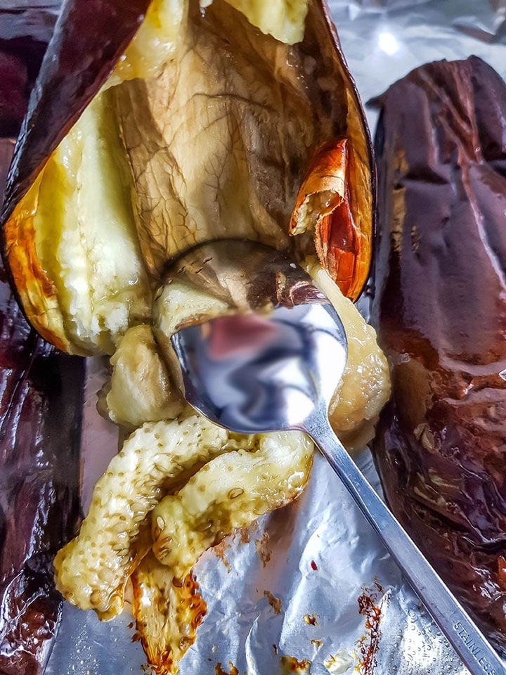 The flesh of the eggplant being scraped out of the skin with a spoon