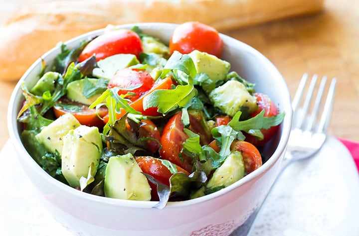 A bowl of bright and colorful tomato avocado salad with some bread in the background.