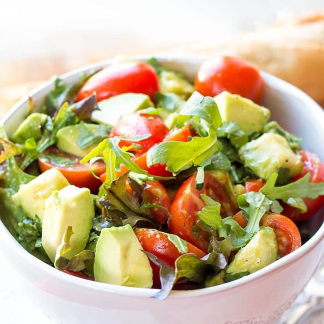 a bowl of the vibrant and colorful tomato avocado salad with some bread in the background