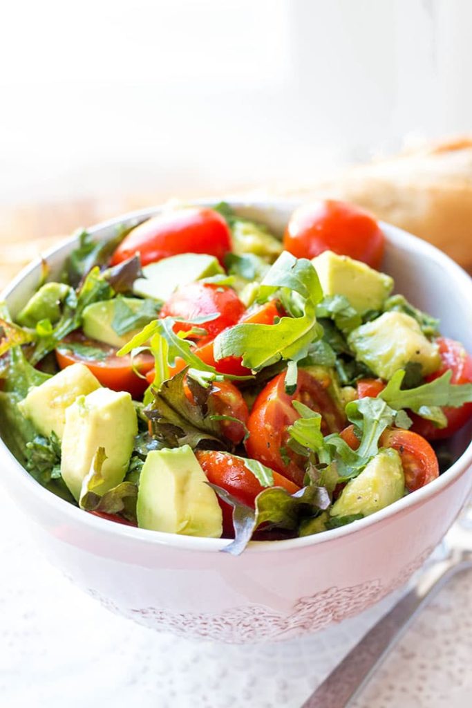 a bowl of the vibrant and colorful tomato avocado salad with some bread in the background