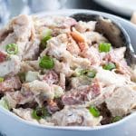 The chicken salad mixed together in a bowl scatted with green onions.