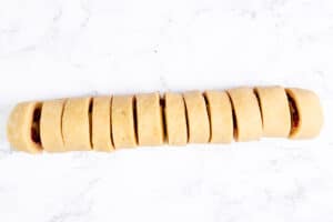 Rolled scone dough with raspberry filling cut into slices, arranged on a marble surface.
