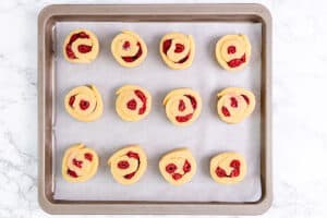 Raspberry-filled scone dough arranged on a parchment-lined baking tray, ready to go into the oven.