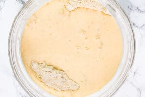 Beaten eggs and cream, mixed in a clear glass bowl, half combined with the dry flour mixture,