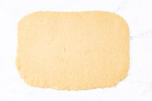 Scone dough rolled out into a rough rectangle shape on a white marble surface.