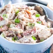 a bowl of chicken salad garnished with sliced green onions and sliced of bread next to it