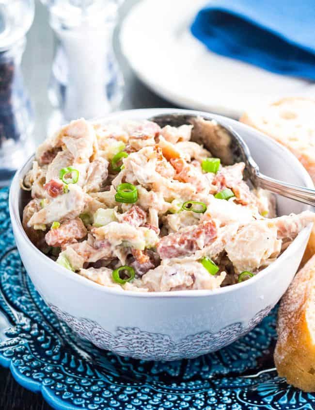 a bowl of chicken salad garnished with sliced green onions and sliced of bread next to it