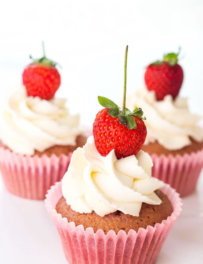 Three fresh strawberry cupcakes all topped with a swirl of whipped cream and a fresh strawberry