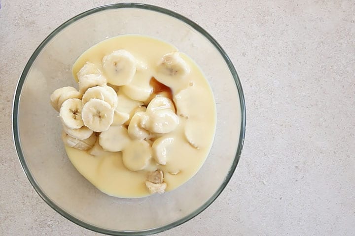 A glass bowl with sliced bananas, condensed milk and vanilla extract.