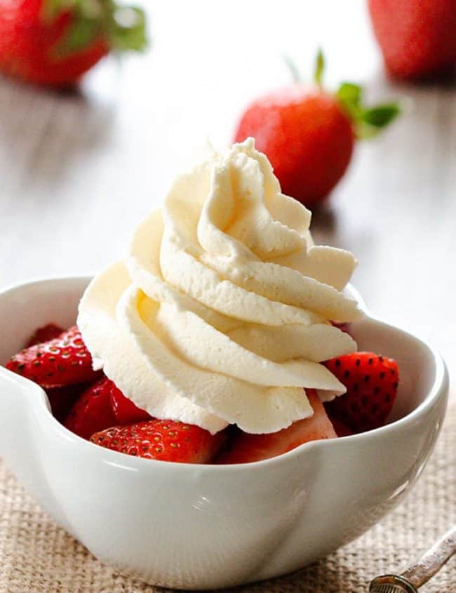 A bowl of strawberries topped with fresh whipped cream