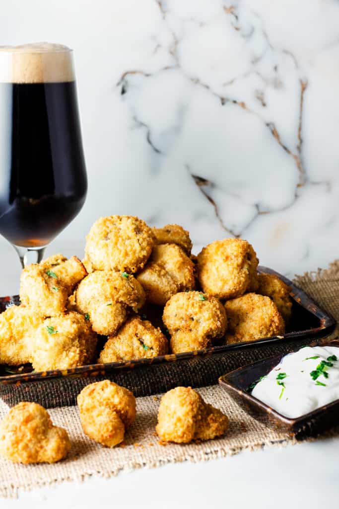 A plate of breaded and baked garlic mushrooms next to a glass of beer.