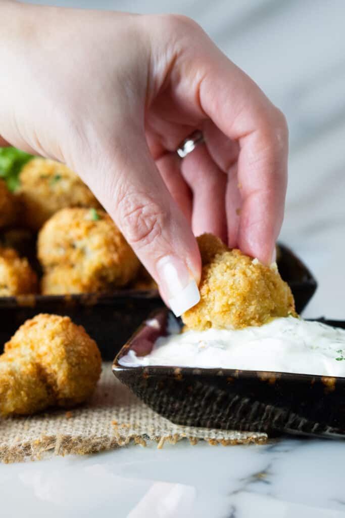 A close-up of a hand dipping a fried mushroom into a white dipping sauce.