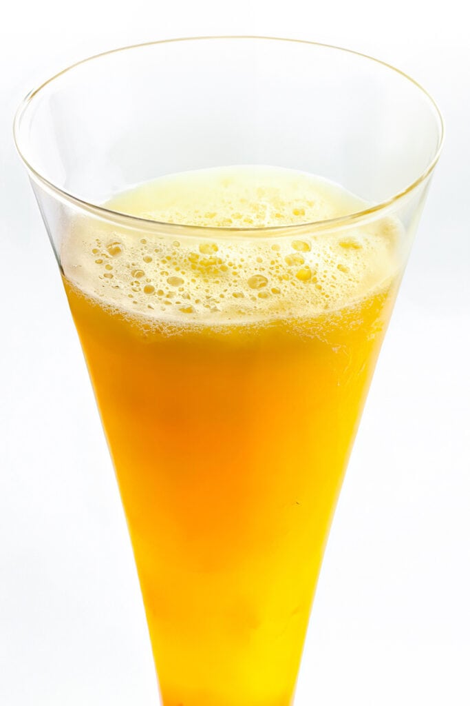 A glass of Peach Bellini cocktail with a fizzy foam top.