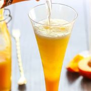 Prosecco being poured into the peach puree in a flute glass to finish off the Bellini Cocktail