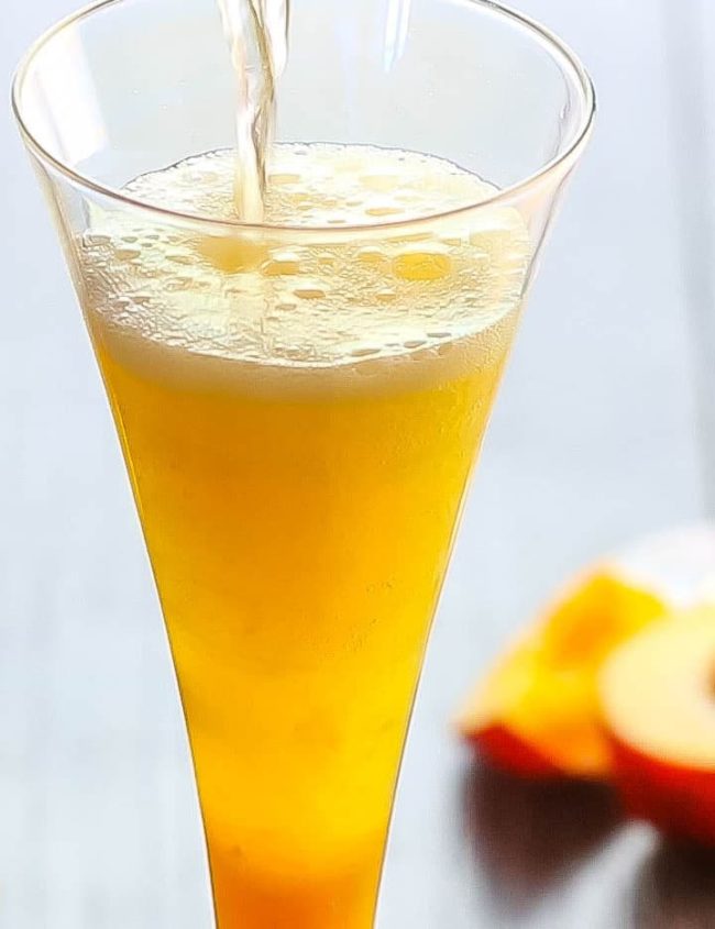 A Bellini Cocktail with fizzy Prosecco being poured into it.