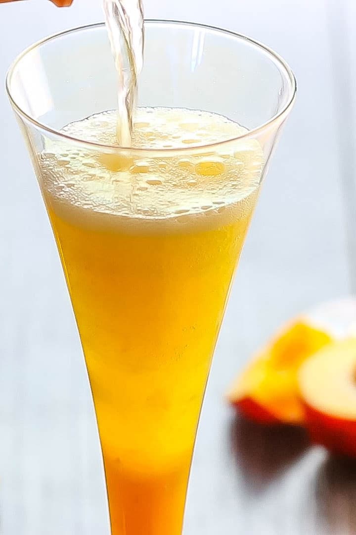 A Bellini Cocktail with fizzy Prosecco being poured into it.