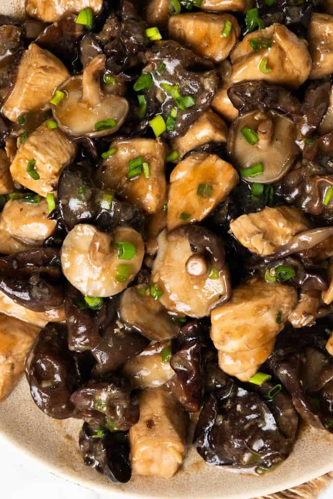 Close-up of a dish featuring Chicken with Chinese Mushrooms, including tender chicken pieces, mushrooms, wood ear fungus, and chopped green onions in a glossy sauce.