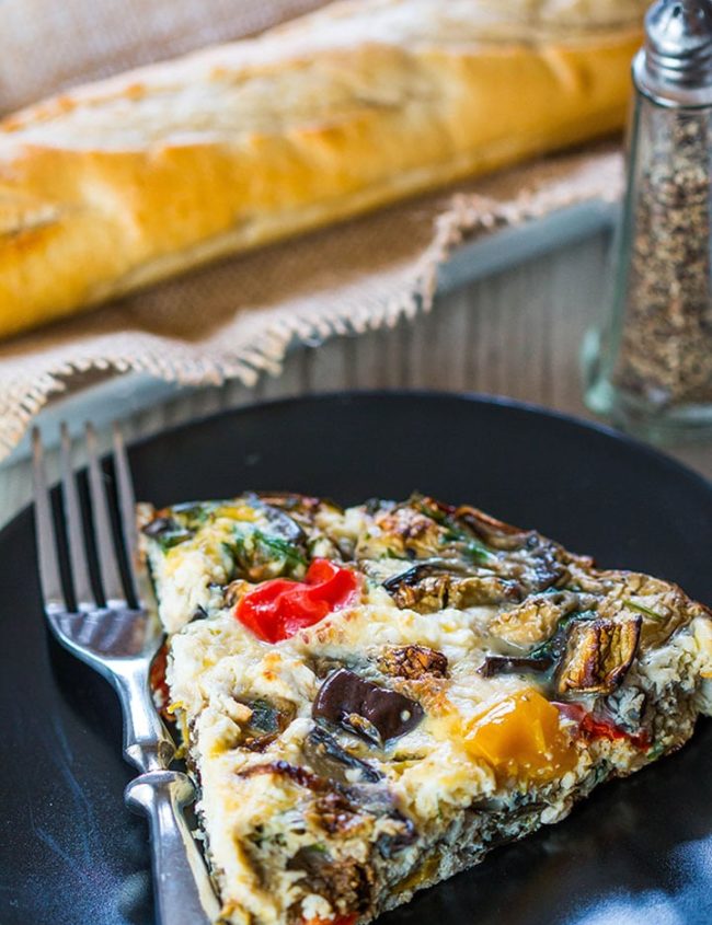 A slice of Baked Eggplant Frittata with Red Onion, Peppers & Feta with bread and salt and pepper in the background