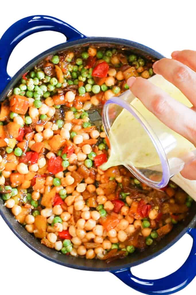 the stock being poured into the pan with the vegetables