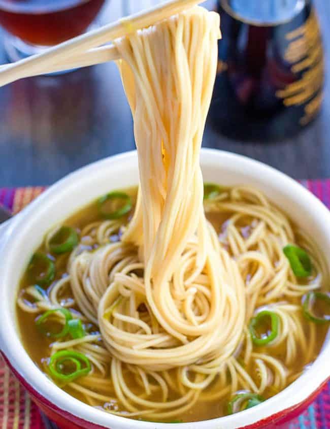 A bowl of quick and easy Chinese noodle soup with chopsticks holding some noodles above the bowl