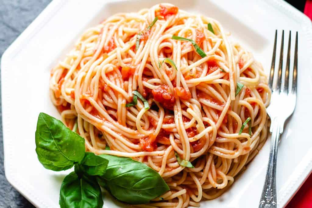 A photo taken from above of a plate of spaghetti with tomato sauce with a fork next to it