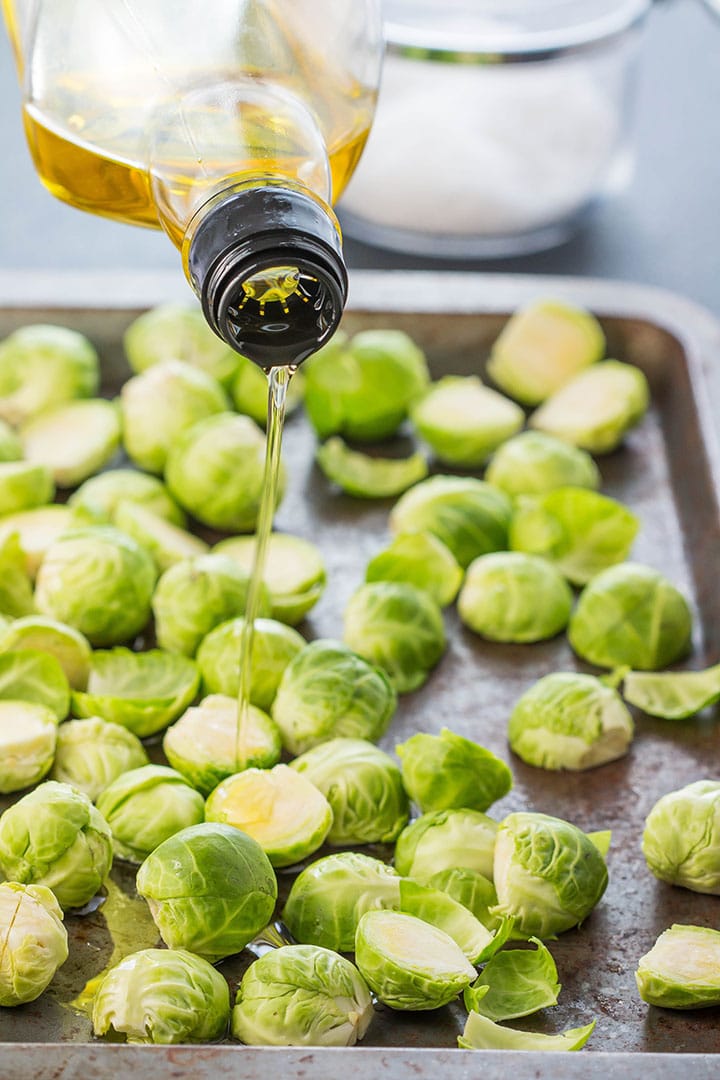 olive oil being poured onto the Brussels Sprouts on a pan