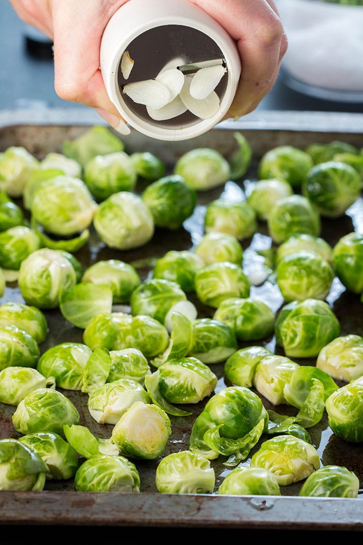 Thinly sliced garlic being cut over the Brussels sprouts