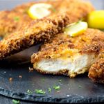 Crispy Breaded Chicken Cutlets on a dish with a piece cut off showing the juicy meat