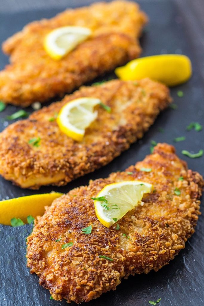 Crispy Breaded Chicken Cutlets on a slate platter sprinkled with parsley and topped with slices of lemon
