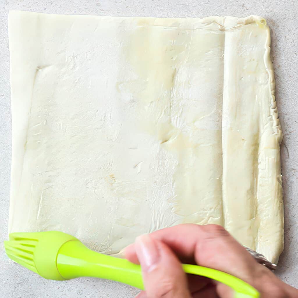 a hand holding a brush to brush the egg wash onto the edges of the dough.