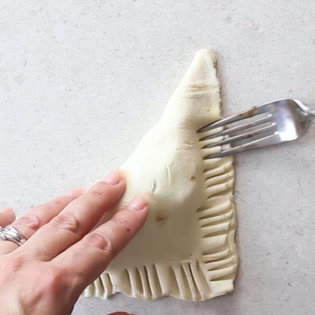 a fork pressing the edges of the turnover to seal the dough.