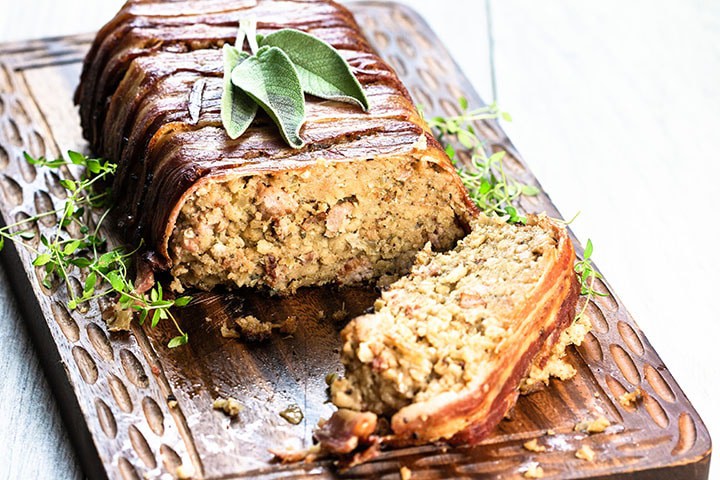 Bacon Wrapped Sausage Stuffing with a slice cut out of it showing the stuffing with sausage meat throughout