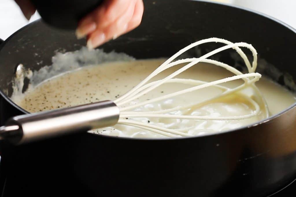 a pepper frinder grinding pepper into the cheese sauce