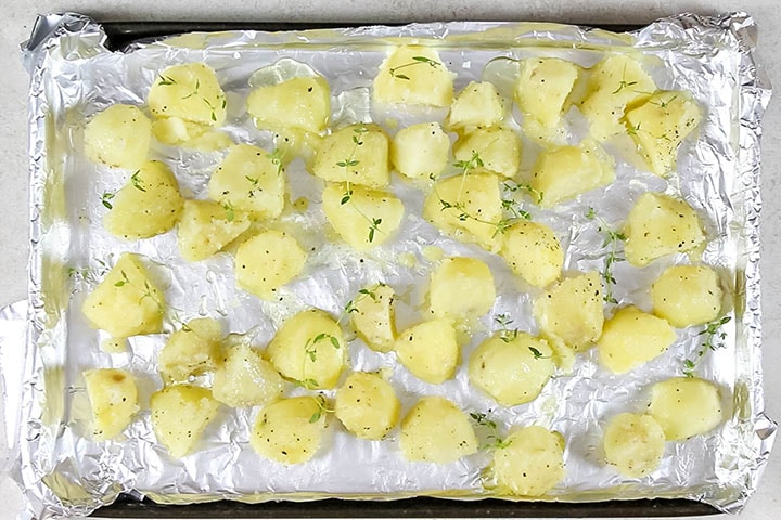 golden roasted potatoes piled high on a dish sprinkled with salt and fresh thyme