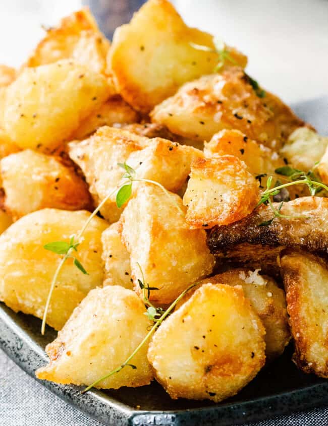 golden roasted potatoes piled high on a dish sprinkled with salt and fresh thyme